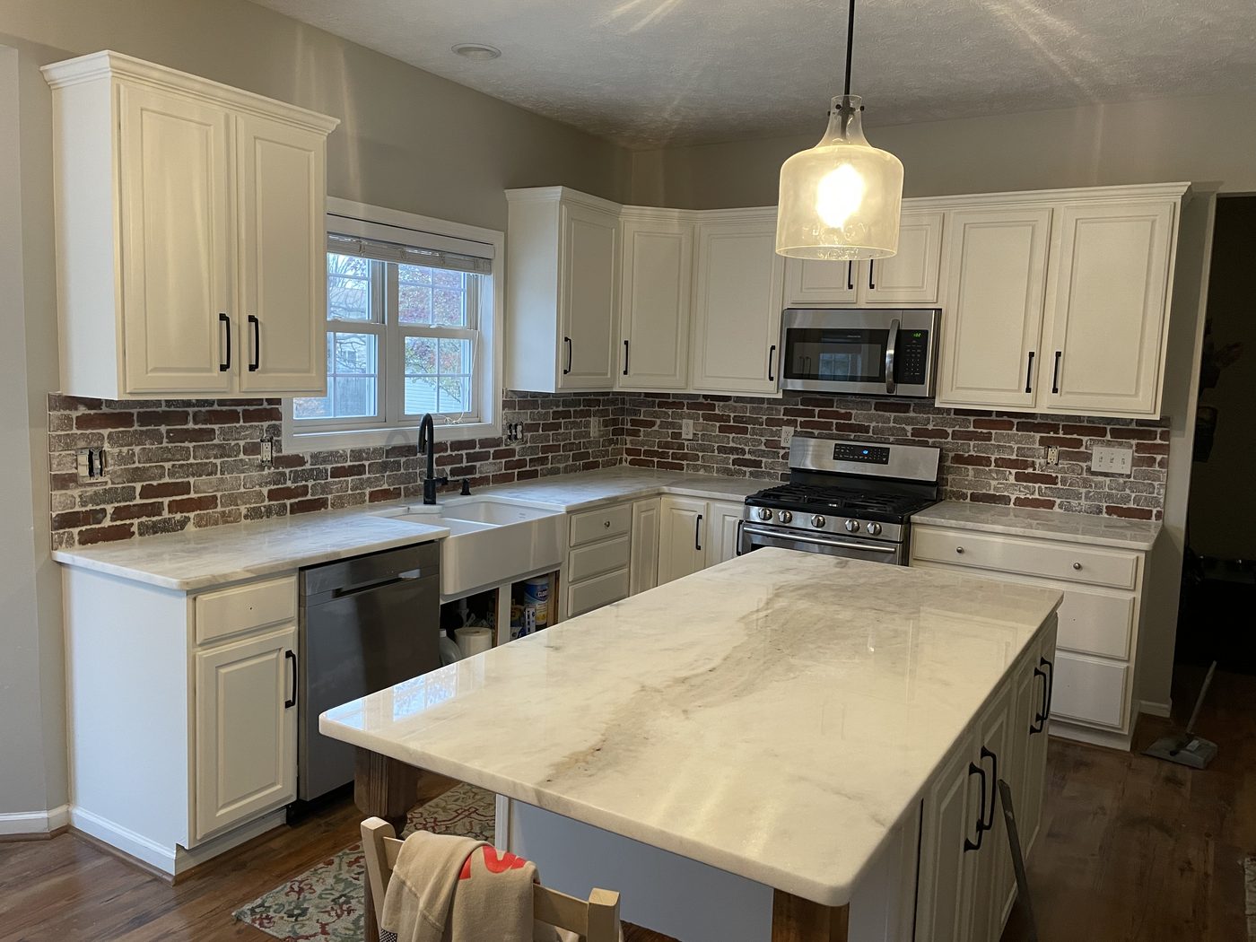 Kitchen remodel with white raised-panel cabinets, exposed red brick backsplash, and marble waterfall island in Northeast Ohio