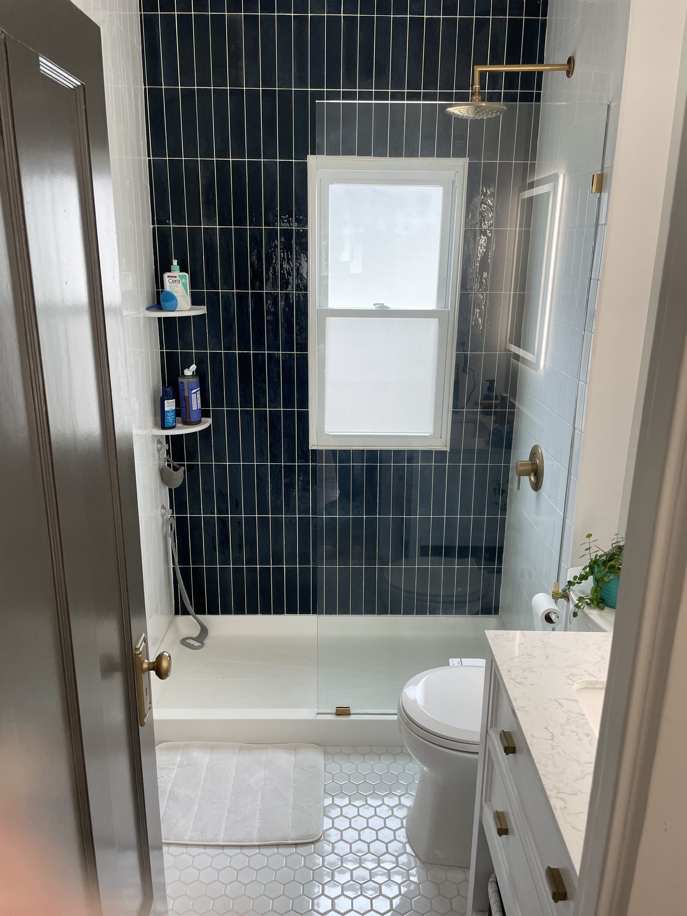 Walk-in shower remodel with navy blue vertical subway tile, white hexagon mosaic floor, and vintage brass fixtures in Lake County Ohio