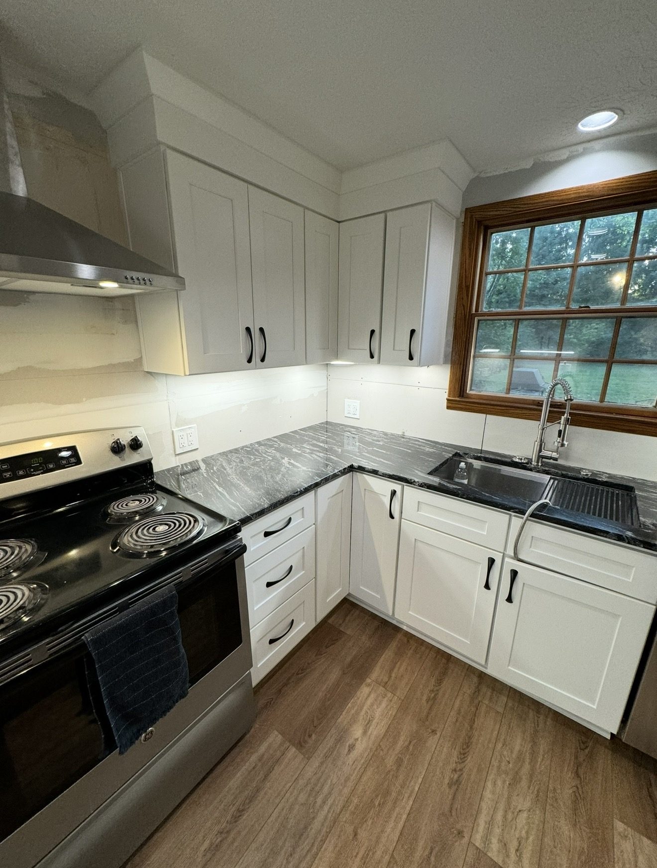Kitchen remodel with white shaker cabinets, dramatic dark veined marble countertops, matte black hardware, and hardwood floors in Lake County Ohio