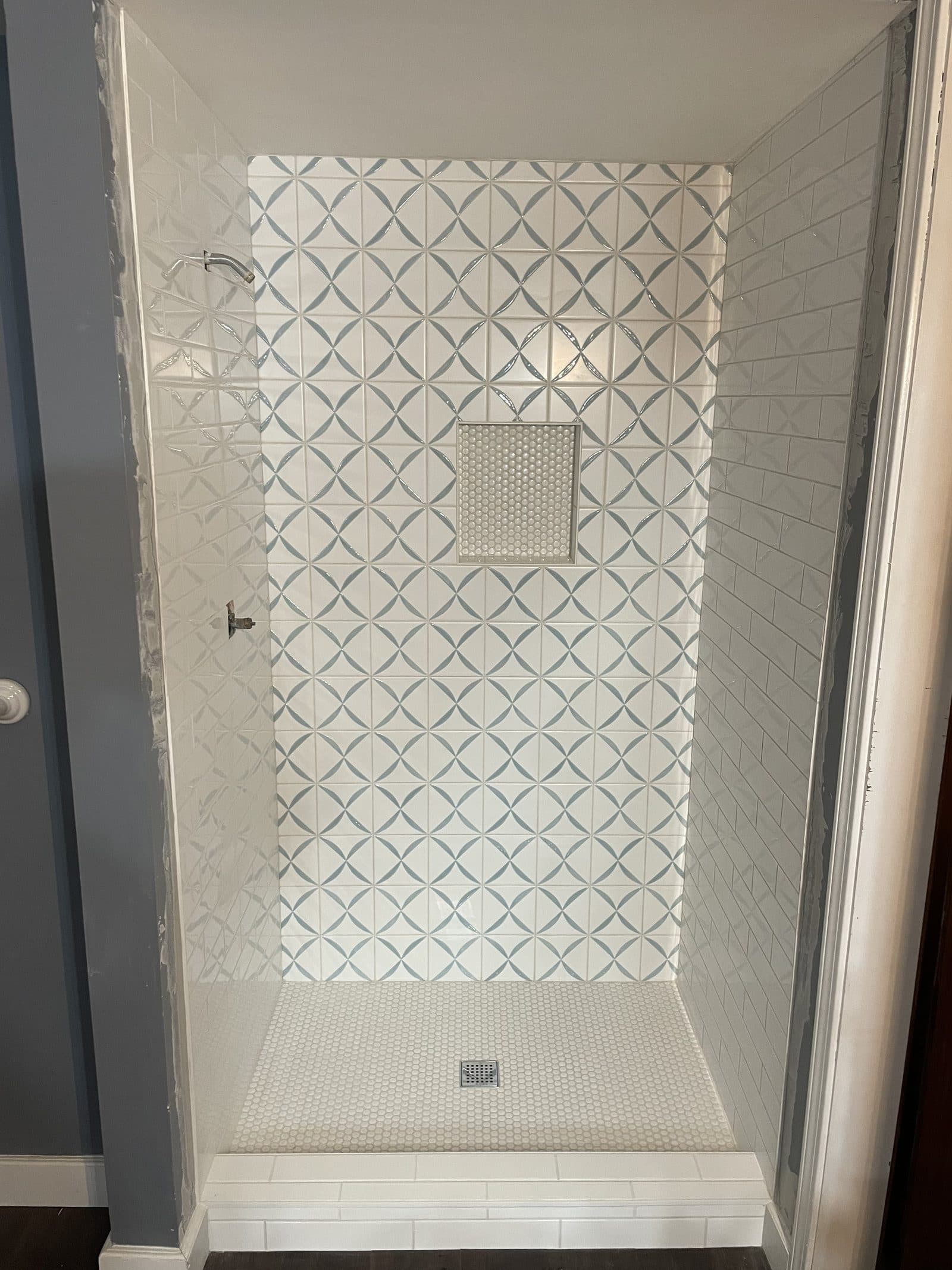 Shower remodel with white geometric pinwheel pattern tile, penny round mosaic niche, and frameless glass door in Cuyahoga County