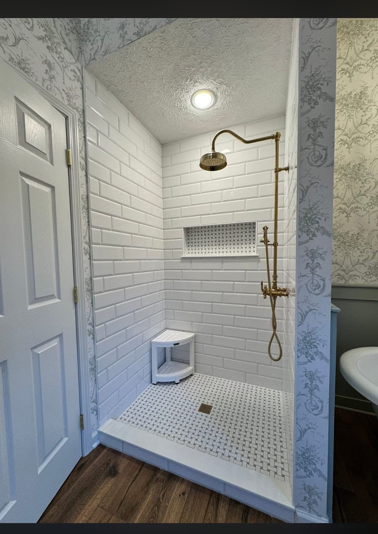Shower remodel with white subway tile, brass vintage-style fixtures, built-in niche, corner bench, and penny mosaic floor in Northeast Ohio