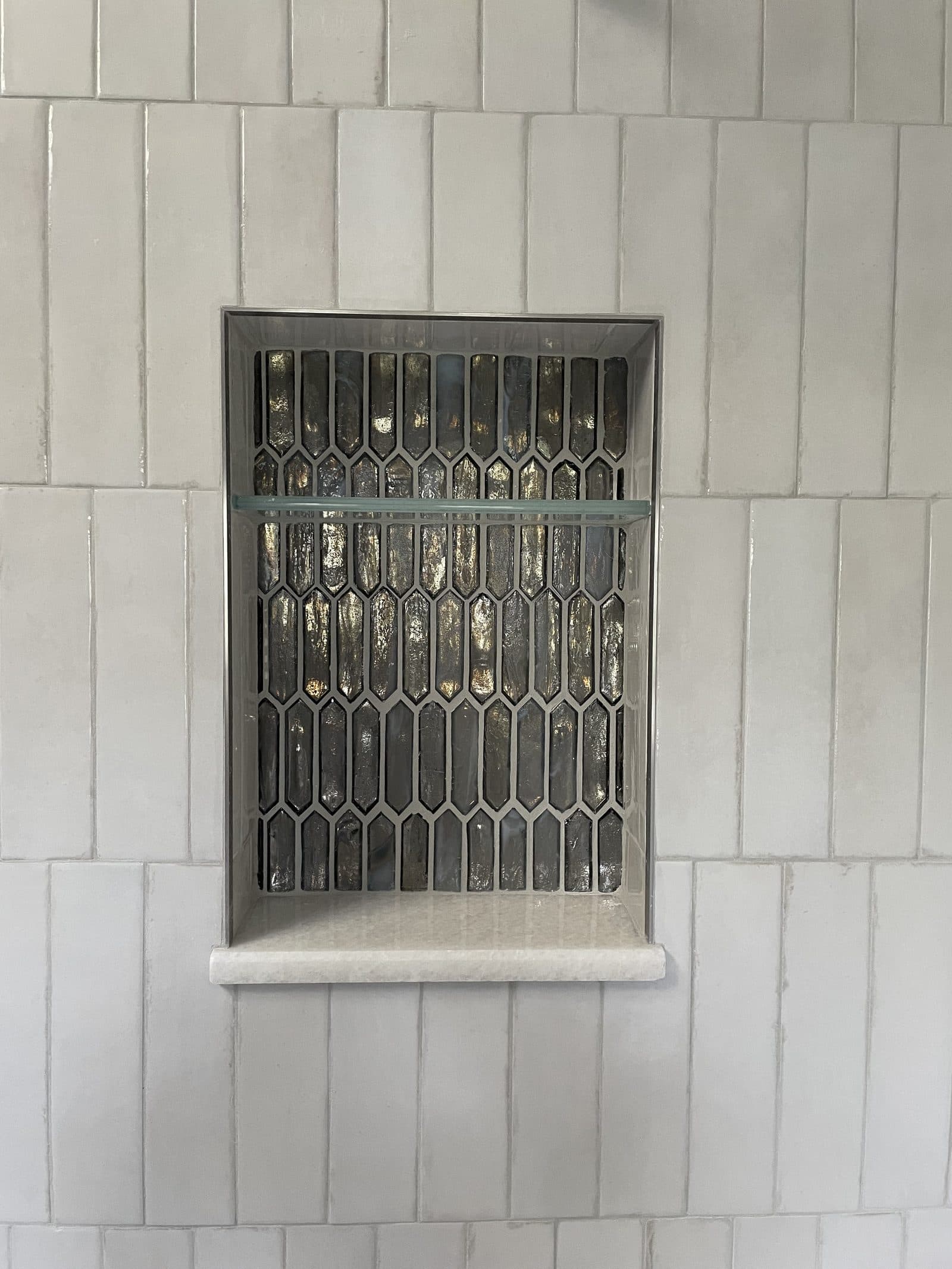 Shower niche detail with dark bronze and gold elongated picket mosaic tile accent and vertical white zellige tile surround in Cuyahoga County