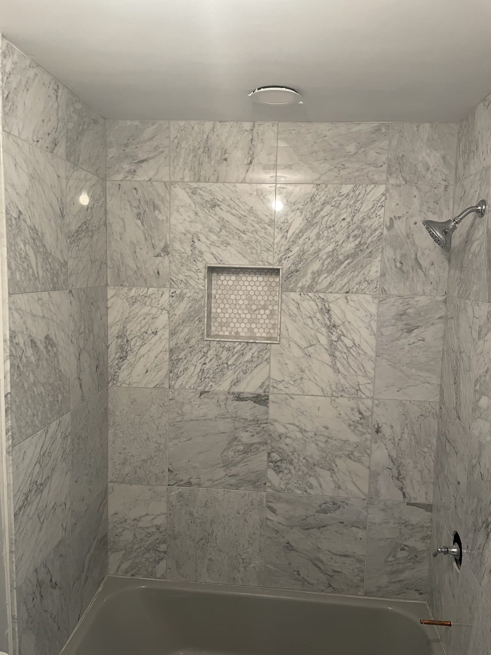 Marble shower and tub surround with large-format marble tiles and hexagon penny mosaic niche in Lake County Ohio