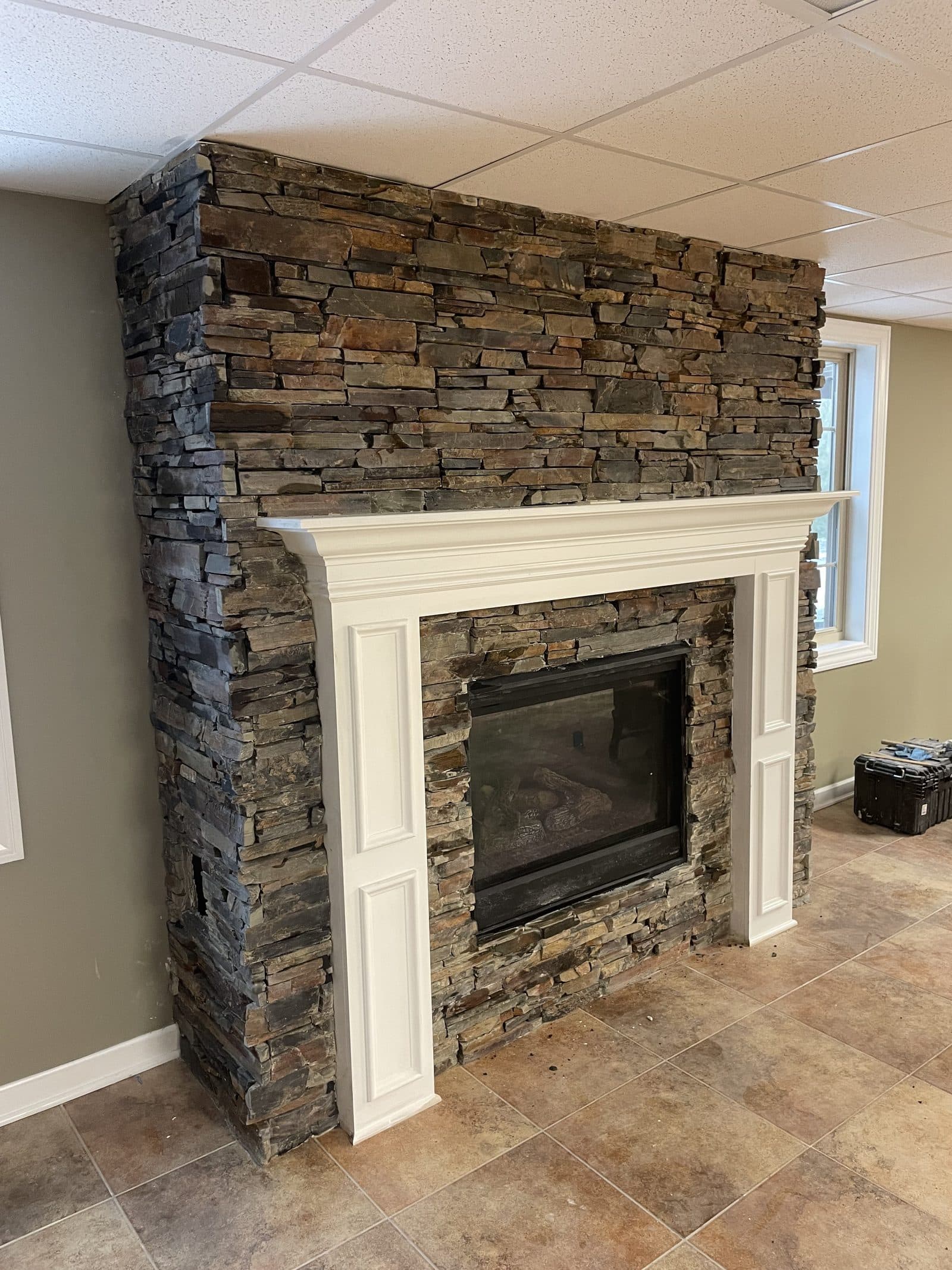 Large stacked natural stone fireplace with white formal mantel surround in basement living area in Northeast Ohio