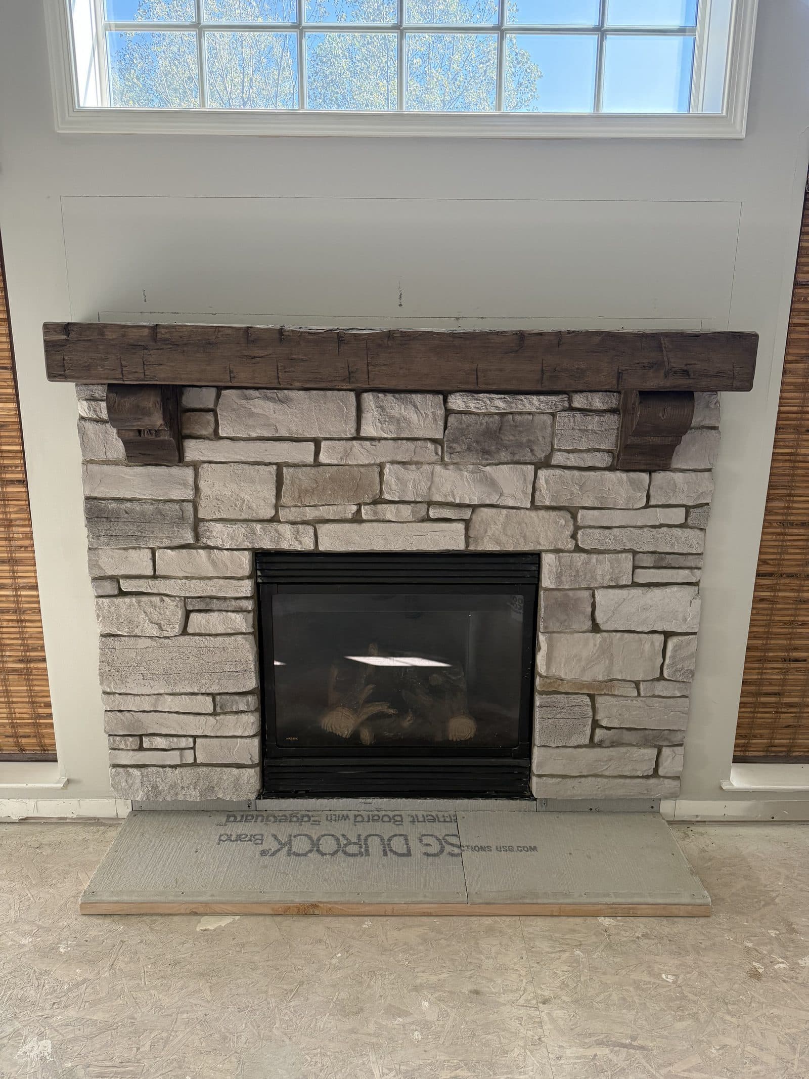 Stacked ledger stone fireplace with rustic reclaimed wood beam mantel and large window above in Lake County Ohio