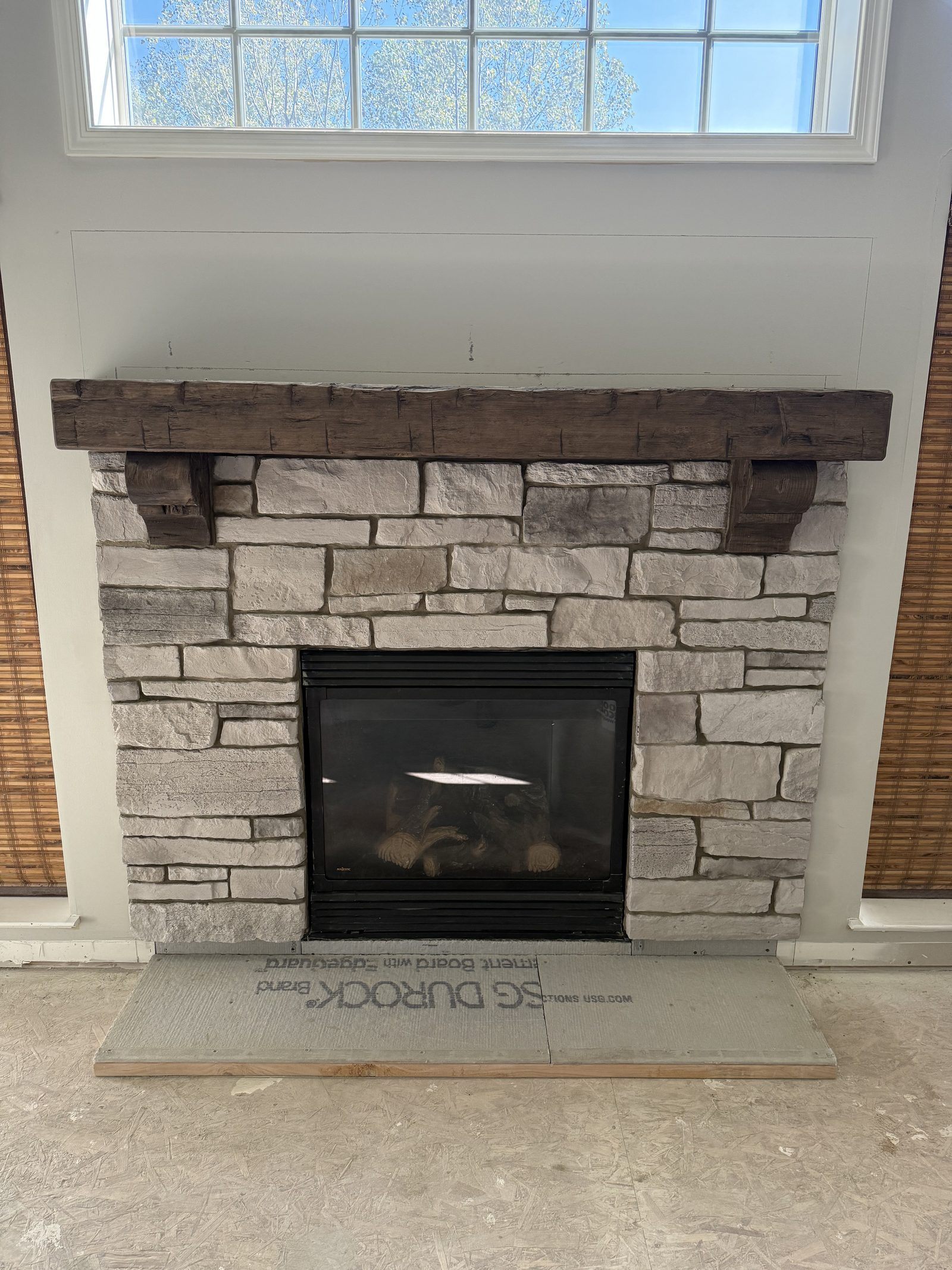 Stacked ledger stone fireplace with rustic reclaimed wood beam mantel and large window above in Lake County Ohio