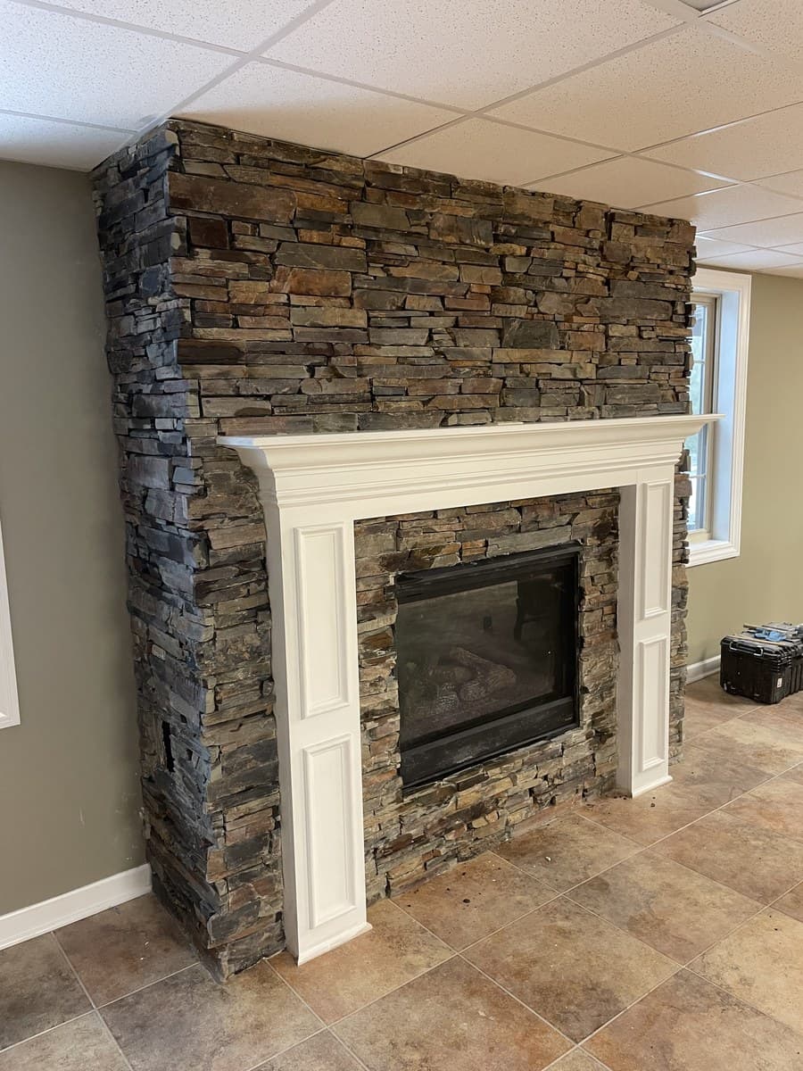 Fireplace remodel with white stacked stone surround and rustic reclaimed wood beam mantel in Lake County Ohio home