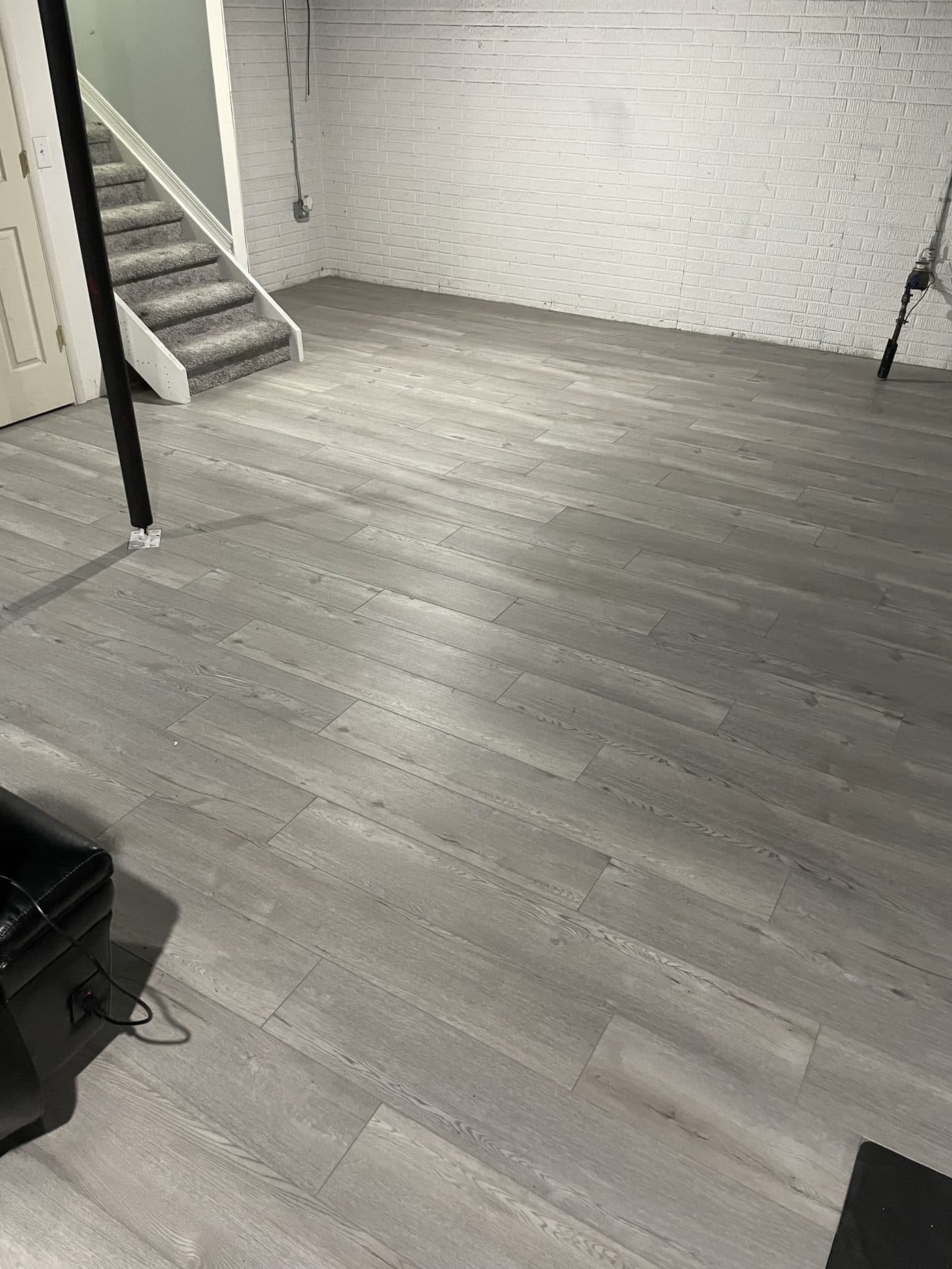 Light grey luxury vinyl plank flooring installation in finished basement with white painted brick in Lake County Ohio