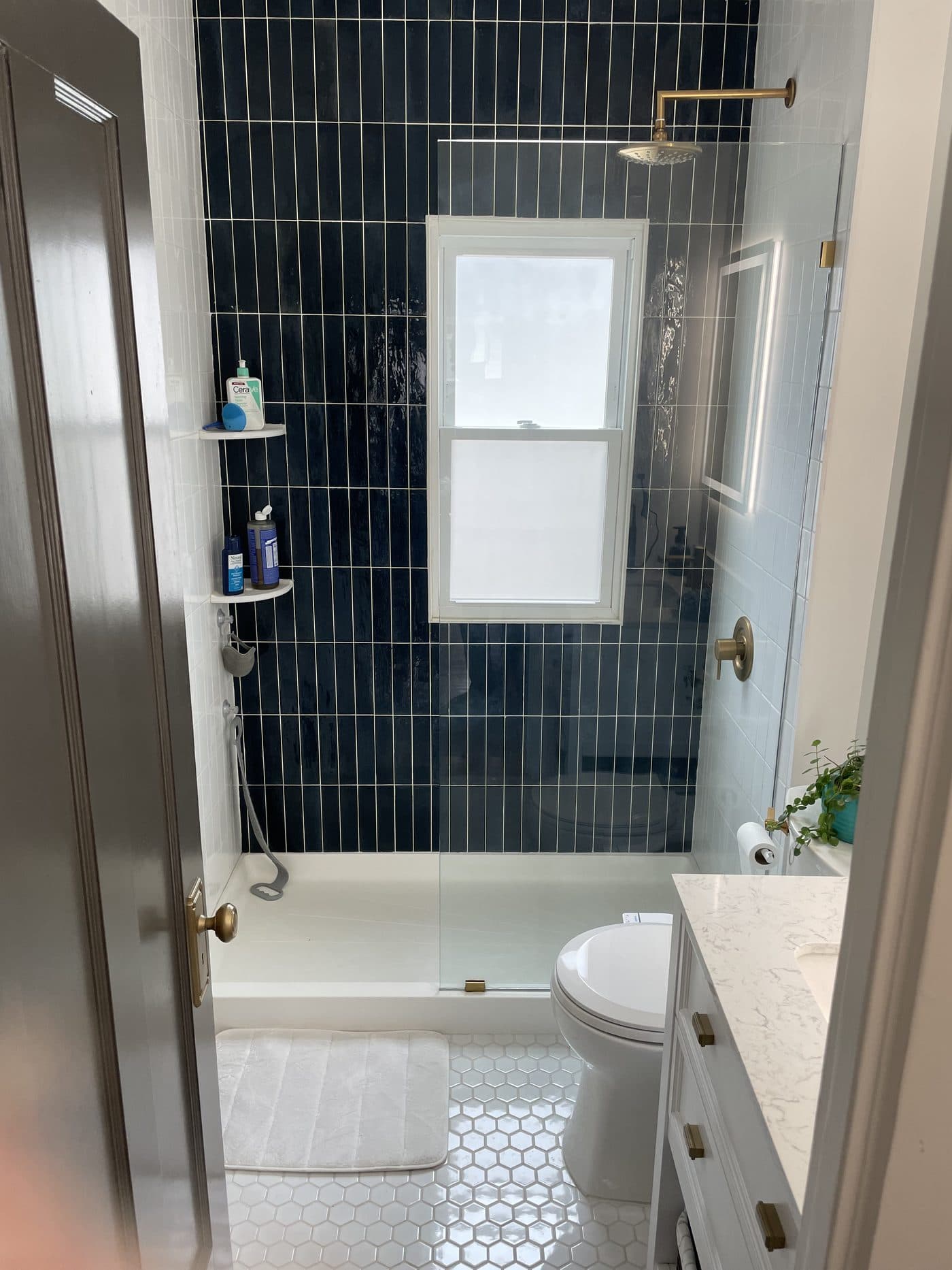 Walk-in shower remodel with navy blue vertical subway tile, white hexagon mosaic floor, and vintage brass fixtures in Lake County Ohio