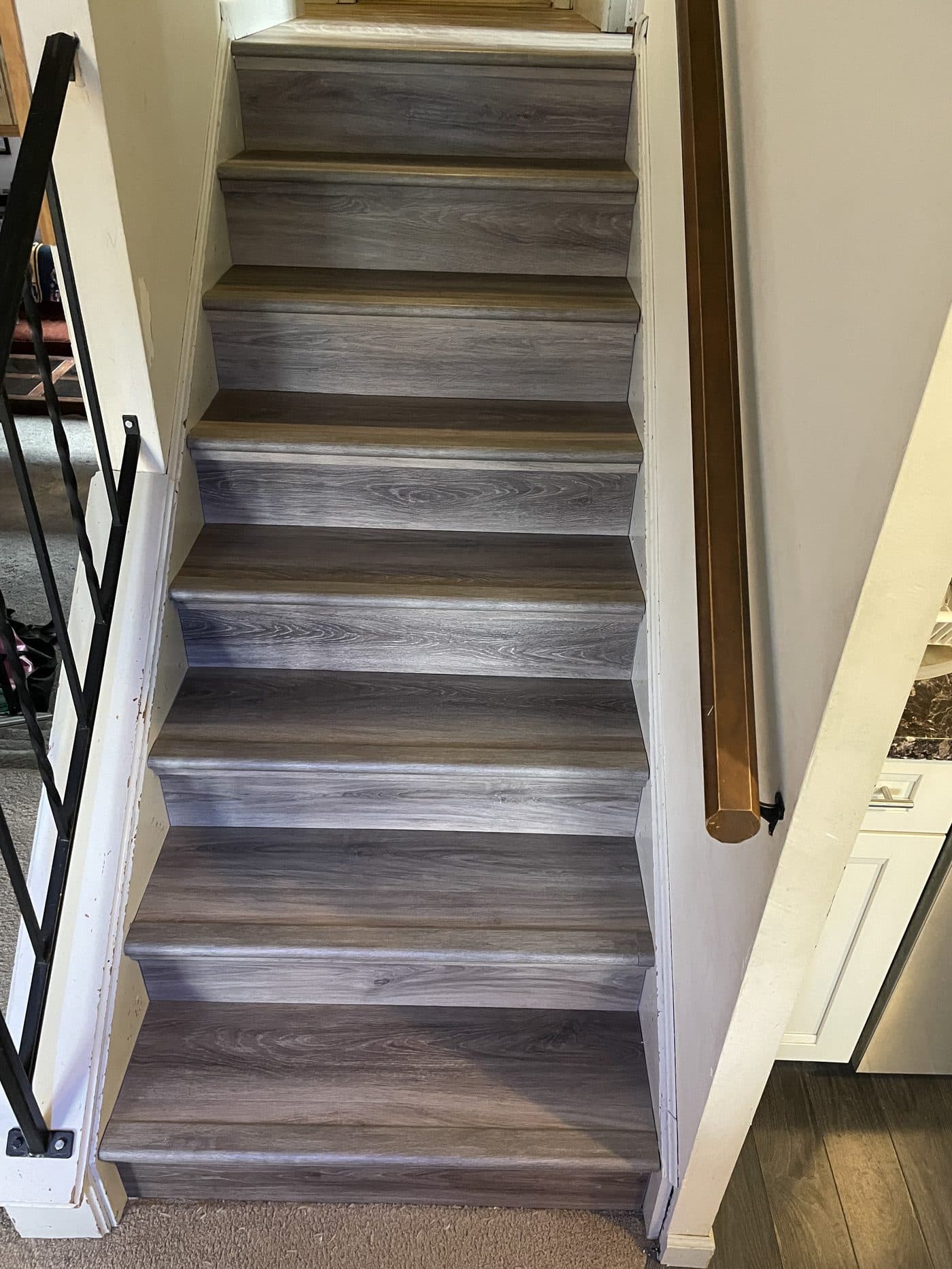 Grey wood-grain luxury vinyl plank stair installation with black iron railing in Northeast Ohio home