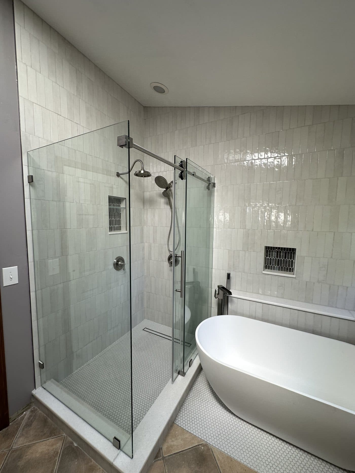 Spa-style master bathroom remodel with white zellige tile, freestanding oval soaking tub, glass-enclosed shower, and penny mosaic floor in Northeast Ohio