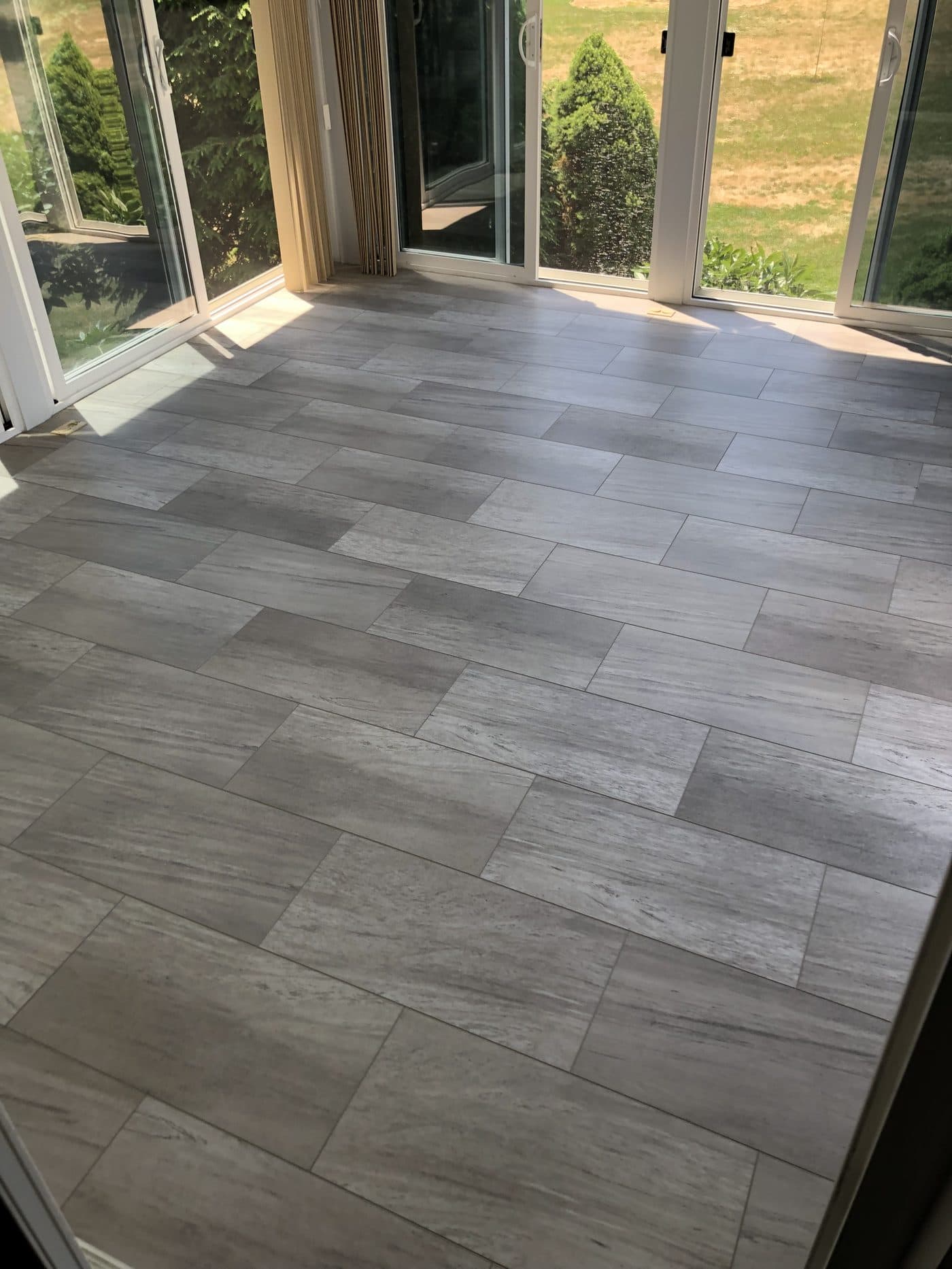 Light grey travertine-look plank tile flooring installation in sunroom addition in Lake County Ohio