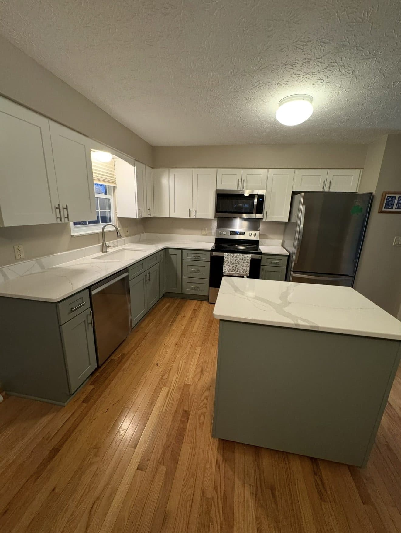 Two-tone kitchen remodel with sage grey lower and white upper cabinets, Calacatta quartz countertops, and oak hardwood floors in Lake County Ohio