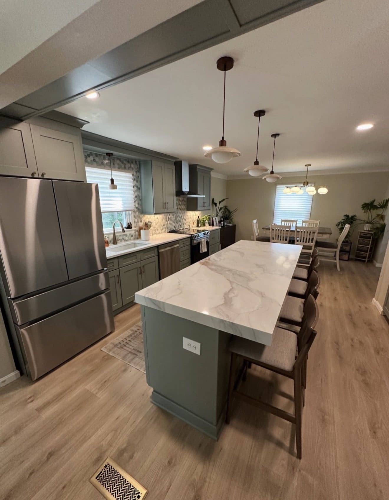 Styled kitchen remodel with olive green cabinets, Calacatta quartz waterfall island, pendant lights, mosaic backsplash, and black range hood in Northeast Ohio