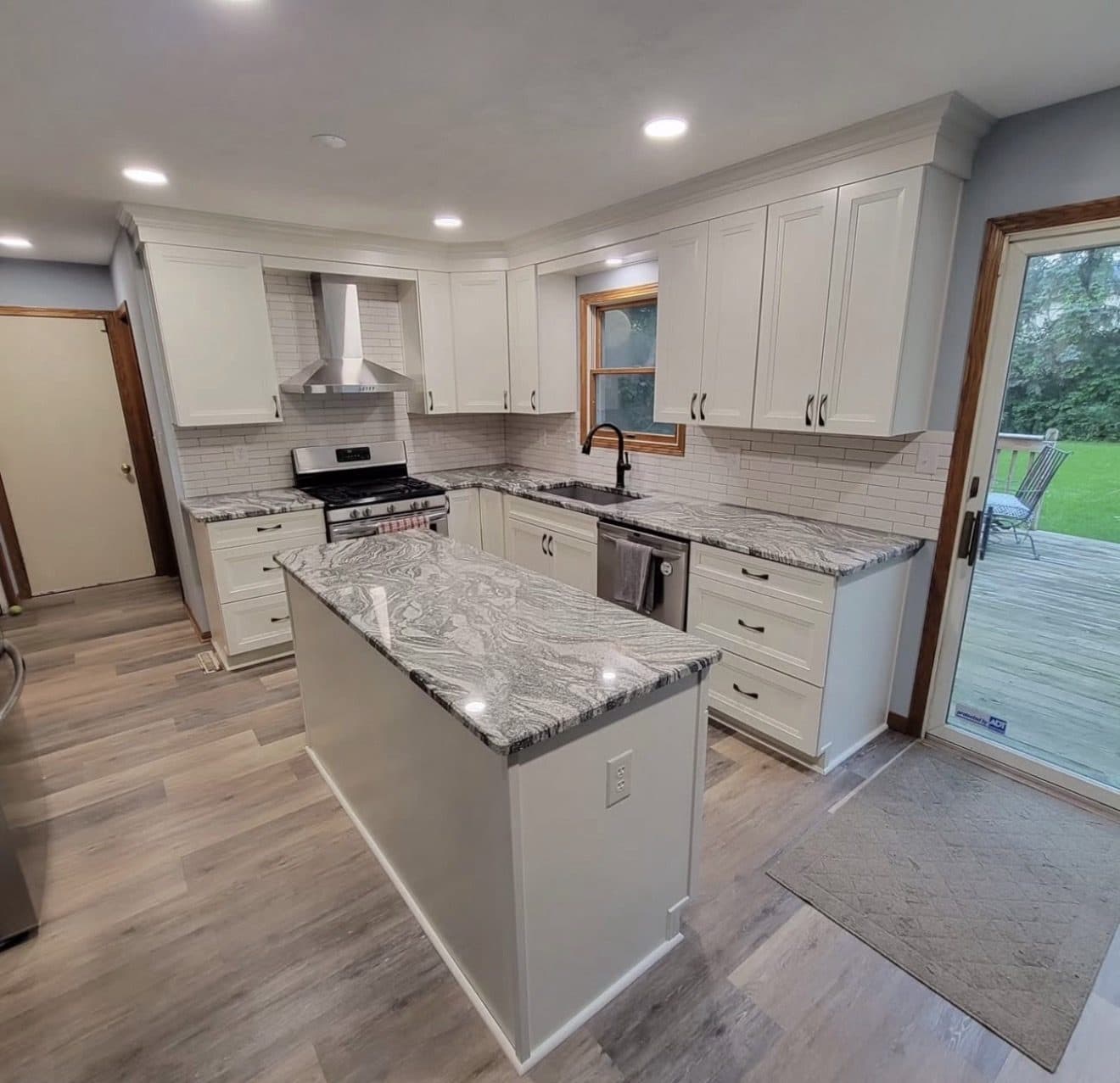 Kitchen remodel with white shaker cabinets, bold swirled grey-and-black granite countertops, white subway backsplash, and black range hood in Northeast Ohio