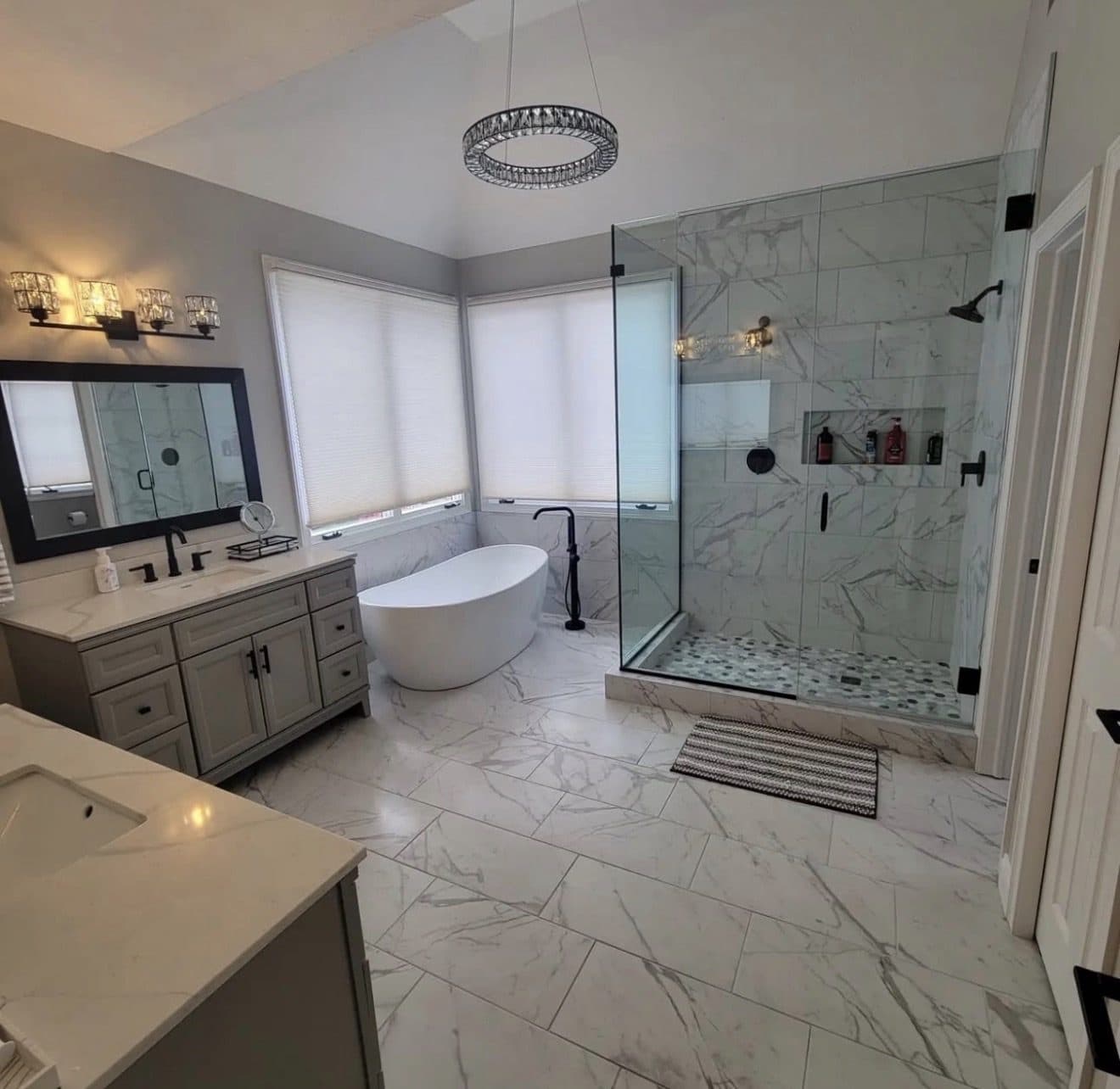 Luxury master bathroom remodel with full Calacatta marble tile floor, freestanding soaking tub, frameless glass walk-in shower, double grey vanity, and crystal chandelier in Lake County Ohio