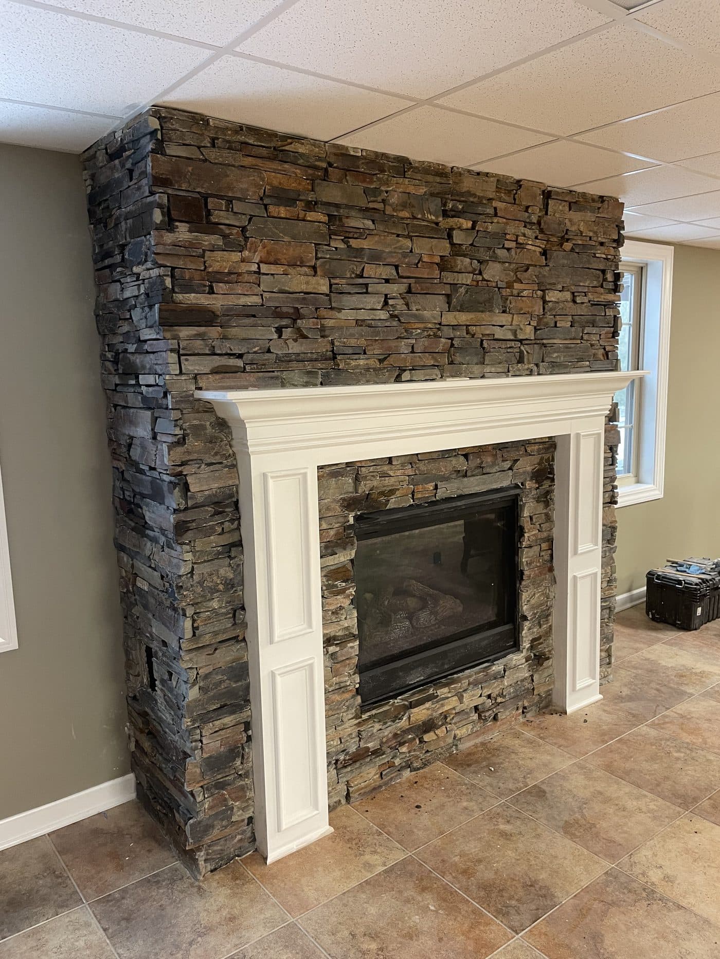 Large stacked natural stone fireplace with white formal mantel surround and built-in cabinetry in finished basement in Lake County Ohio