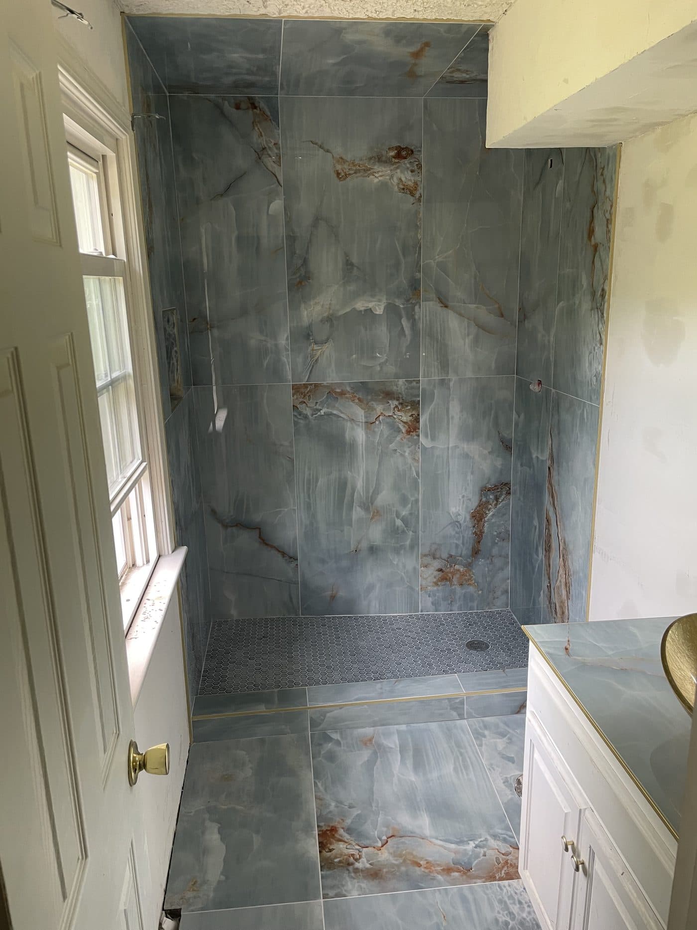 Dramatic shower remodel with bold blue onyx-look porcelain tile walls and frameless glass enclosure in Cuyahoga County