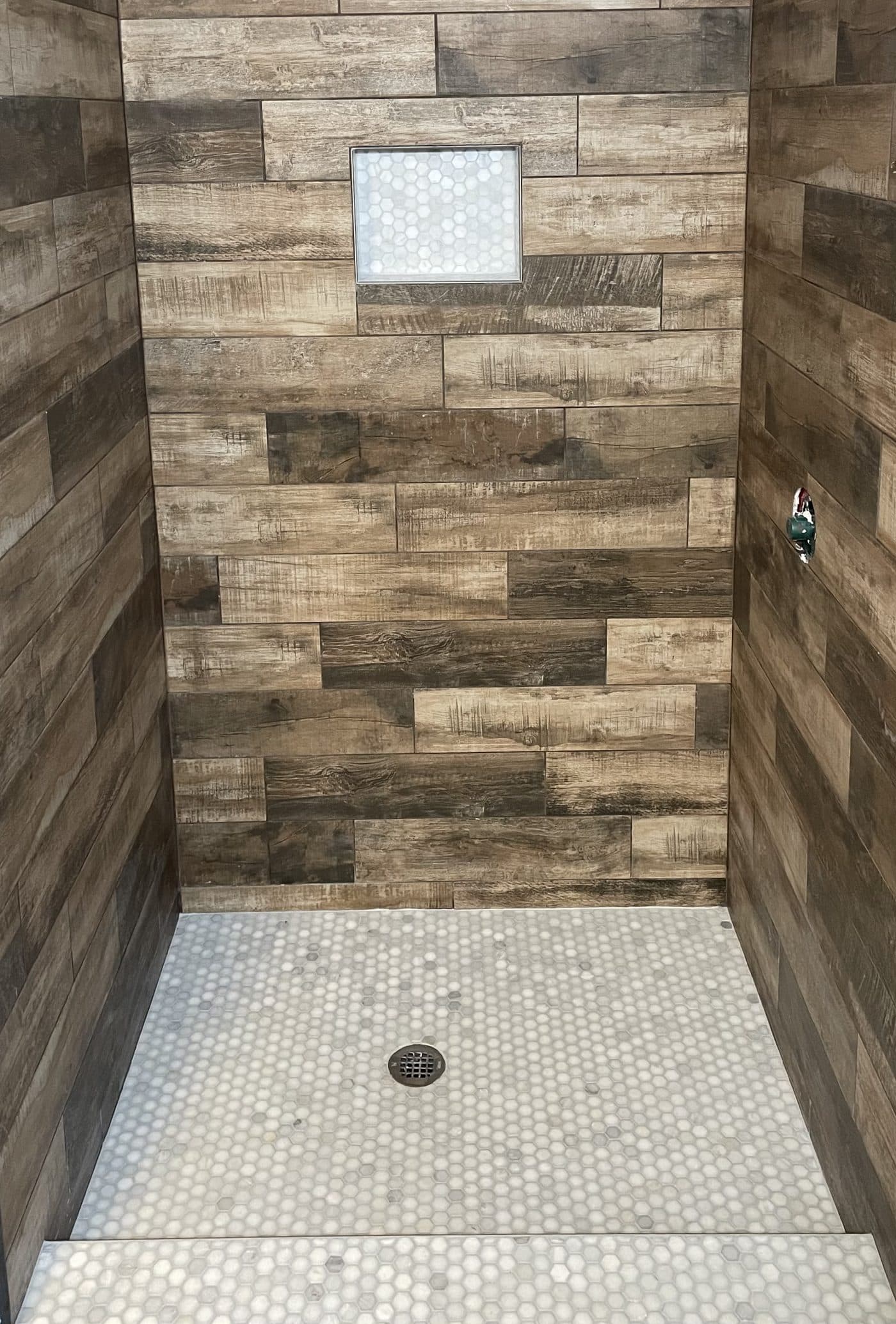 Walk-in shower with wood-look horizontal tile walls, white penny mosaic niche, and hexagon marble floor in Lake County Ohio