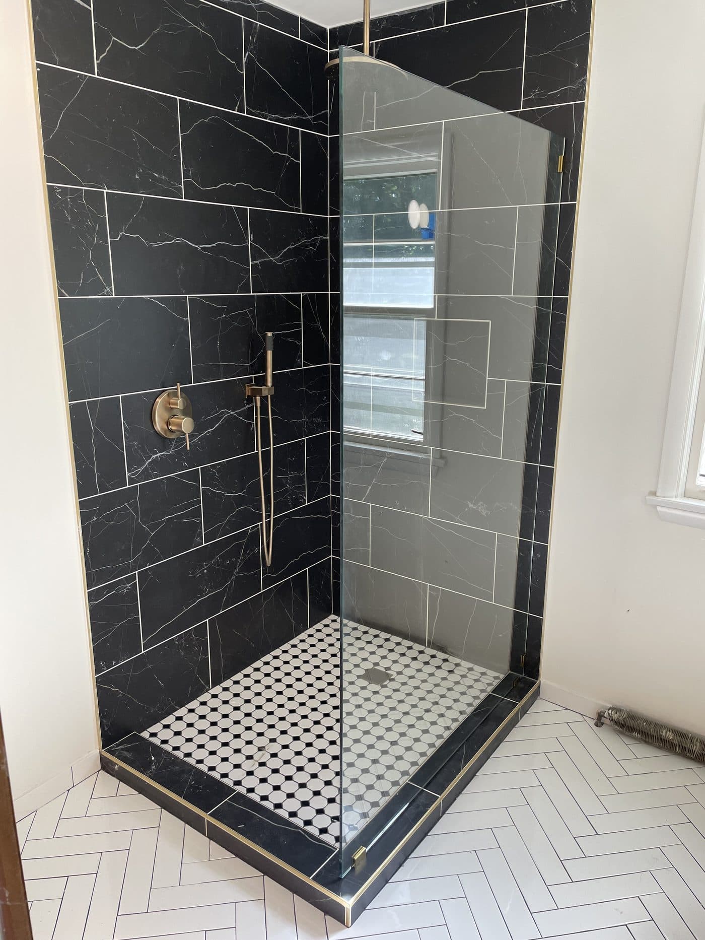Dramatic walk-in shower with bold black marble tile walls, vintage brass fixtures, and octagon mosaic floor in Lake County Ohio