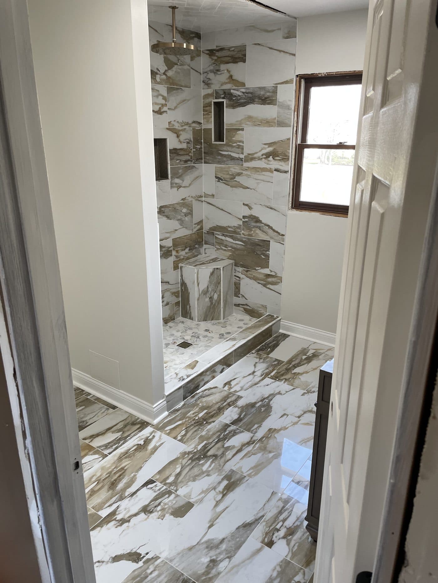 Luxury walk-in shower with book-matched marble-look porcelain walls, penny mosaic accents, double niches, and gold rain head in Northeast Ohio