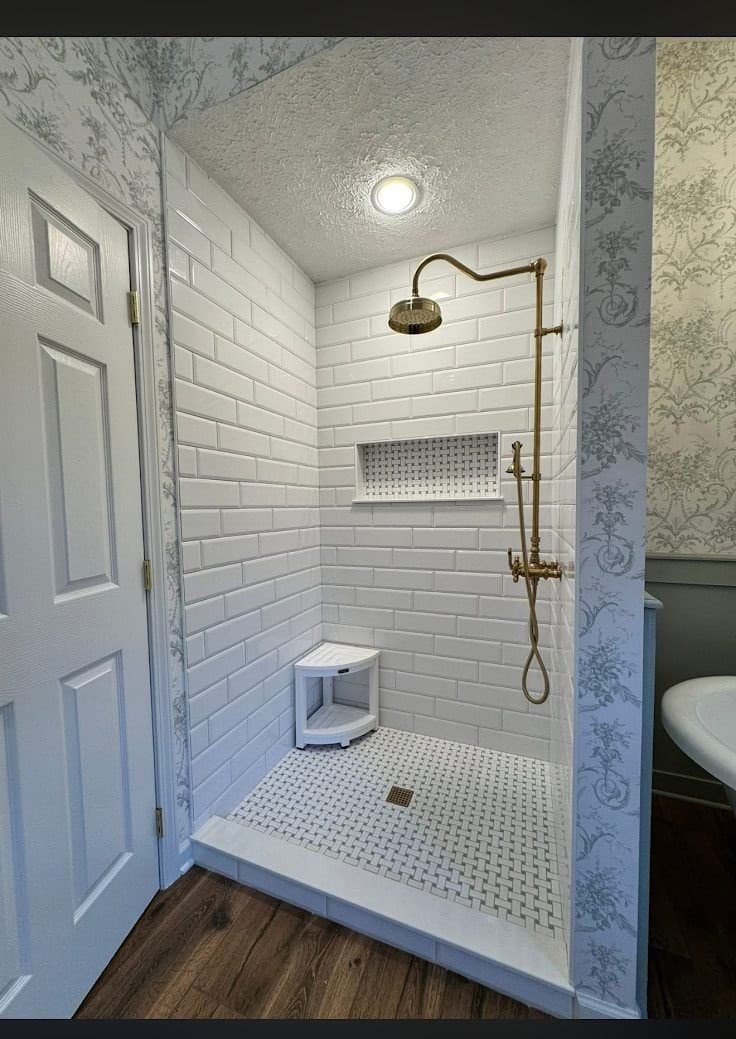 Walk-in shower remodel with white subway tile, vintage brass rain head, penny tile floor, and corner bench in Lake County Ohio